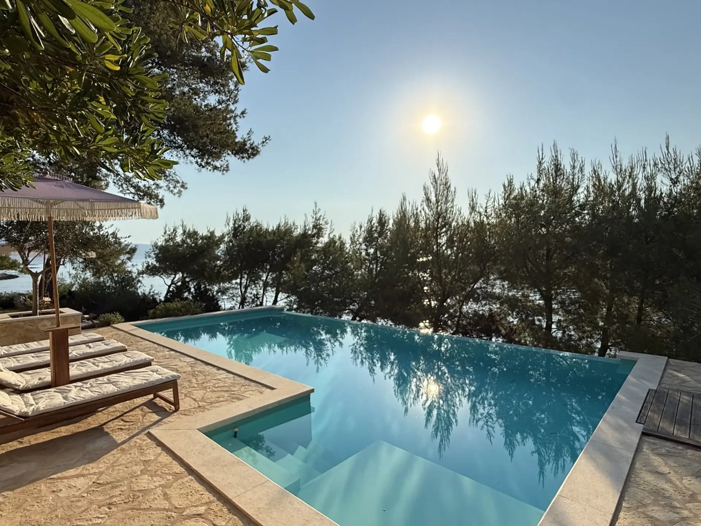 Infinity pool at Villa Aqua with sun over the pines and the sea