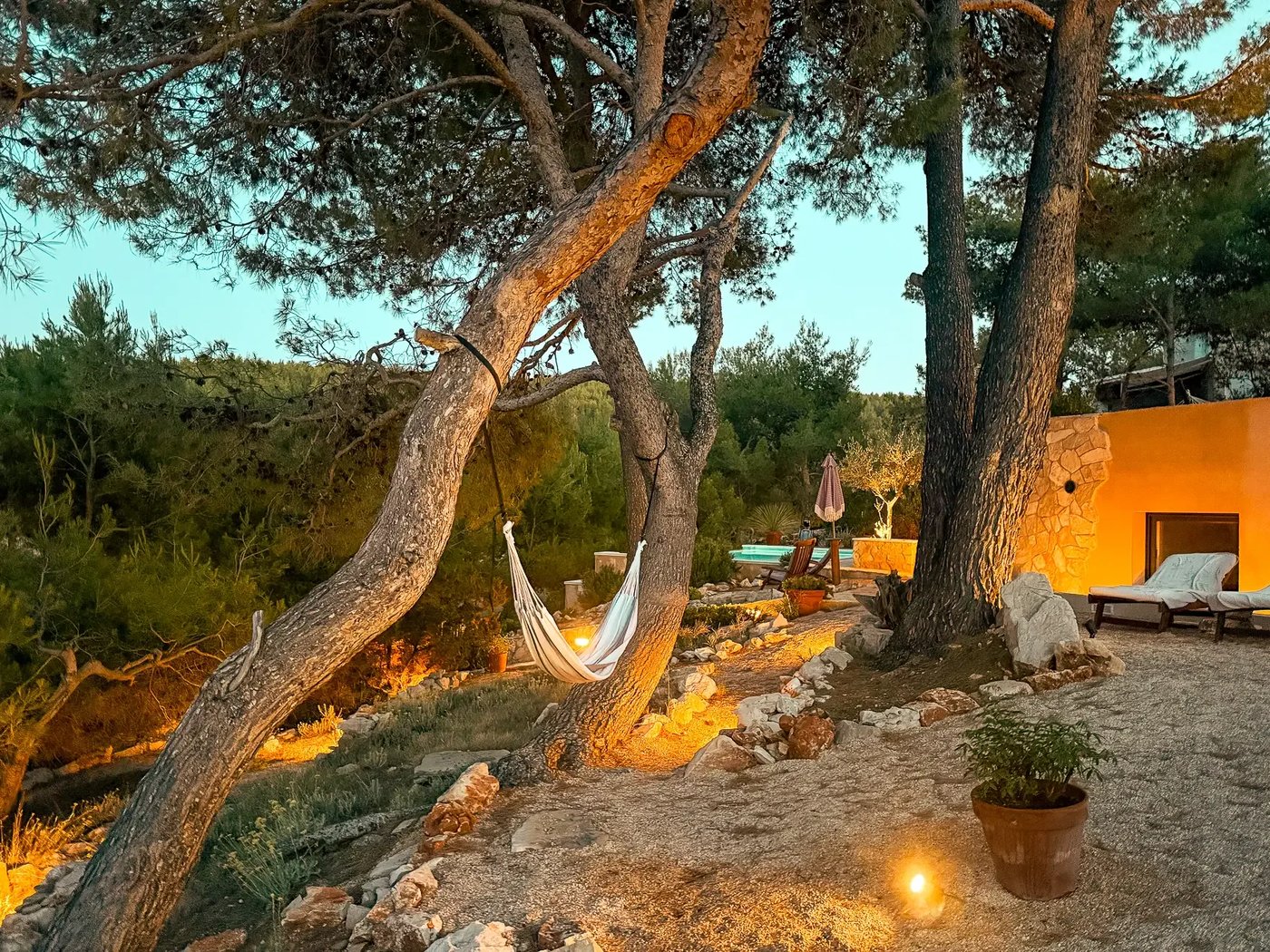 Hammock between pine trees at dusk, lit by warm garden lights